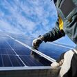 Close up of man technician in work gloves installing stand-alone photovoltaic solar panel system under beautiful blue sky with clouds. Concept of alternative energy and power sustainable resources.