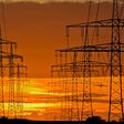 Strommasten und Überlandleitungen vor stimmungsvollem Abendhimmel im Gegenlicht des Nachglühens der untergegangenen Sonne am Horizont
