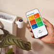 App auf einem Mobiltelefon vor einem Heizkörper, der von einer Wärmepumpe gespeist wird
