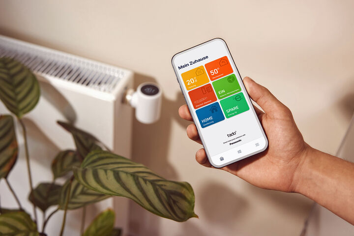 App auf einem Mobiltelefon vor einem Heizkörper, der von einer Wärmepumpe gespeist wird