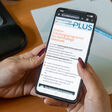 Frau hält Mobiltelefon in der Hand, wo am Bildschirm das Online-Schulungsprogramm für nachhaltige Gebäude zu sehen ist.