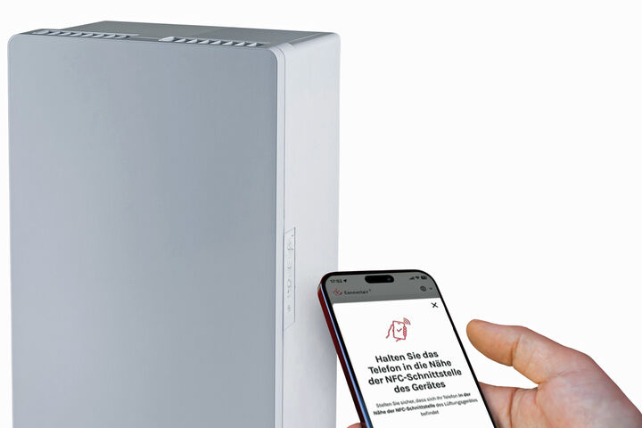 Neues, dezentrales Lüftungsgerät PluggCompact und ein Mobiltelefon, mit dem Fachleute das Gerät (mit App) konfigurieren können.