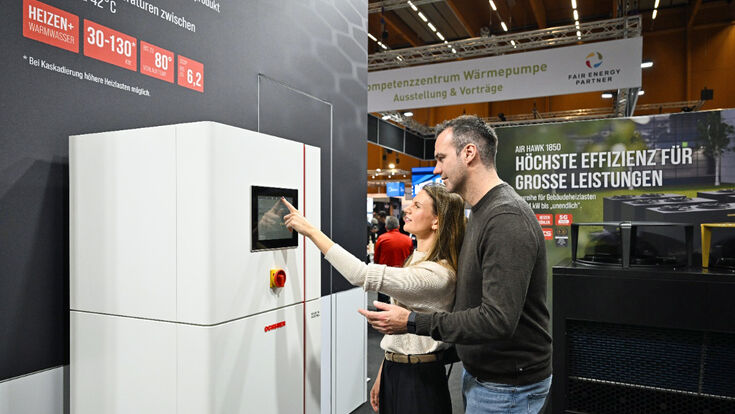 Frau und Mann erkunden bei der Energiesparmesse 2026 die Funktion einer Wärmepumpen-Inneneinheit.