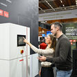 Frau und Mann erkunden bei der Energiesparmesse 2026 die Funktion einer Wärmepumpen-Inneneinheit.