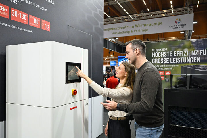 Frau und Mann erkunden bei der Energiesparmesse 2026 die Funktion einer Wärmepumpen-Inneneinheit.