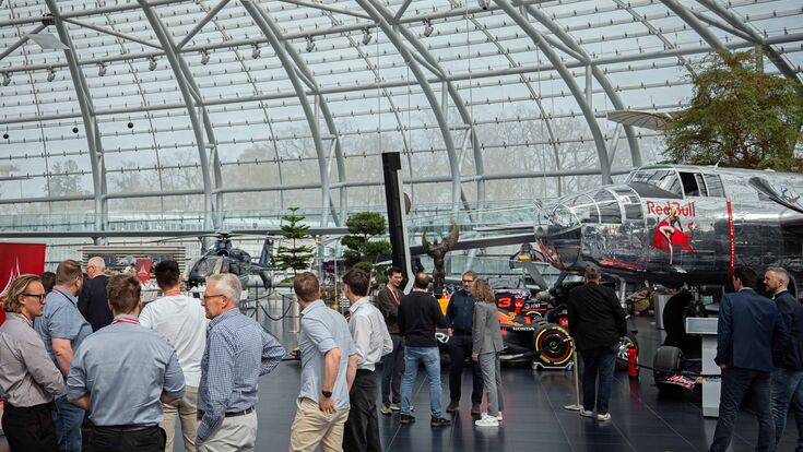 Personen begutachten ein Flugzeug, einen Hubschrauber und ein Formel 1-Auto im Red Bull Hangar-7