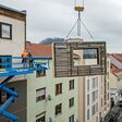 Kran, an dem ein CEPA-Energiefassaden-Element (von TOWERN3000) hängt, das von Monteuren an die Fassade eines Gebäudes angebracht wird.
