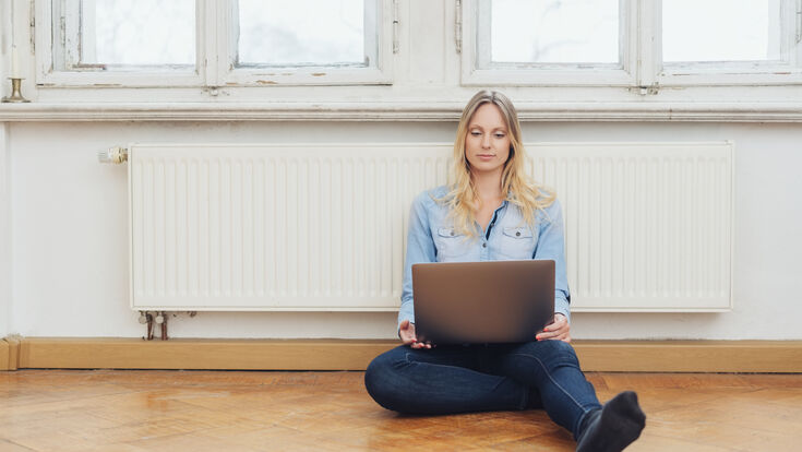 © Adobe Stock girl with laptop sitting on the floor in front of radiator heating system